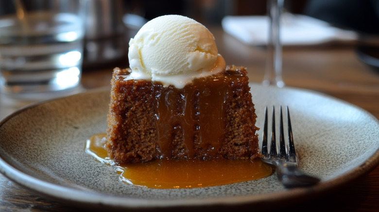 Sticky toffee pudding on plate with scoop of vanilla ice cream on top