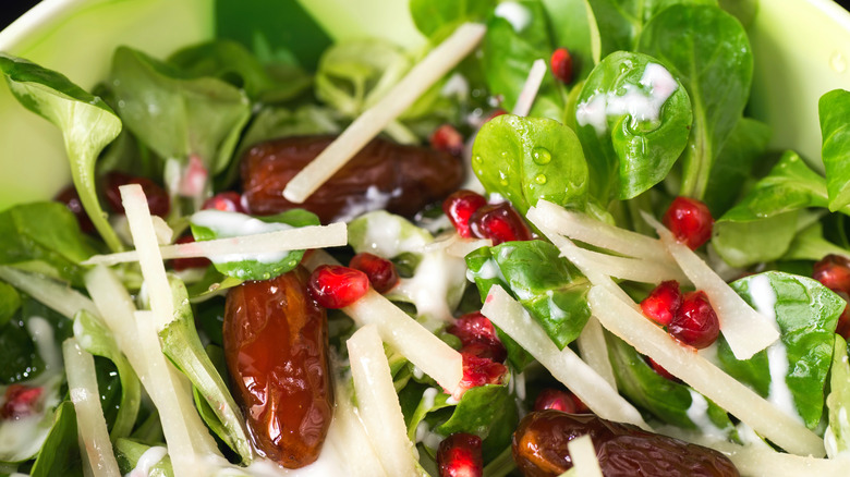 Close up of salad with greens, dates, cheese, and pomegranate seeds