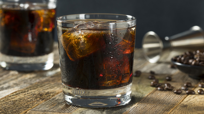 Two black Russians served with ice alongside a jigger and coffee beans