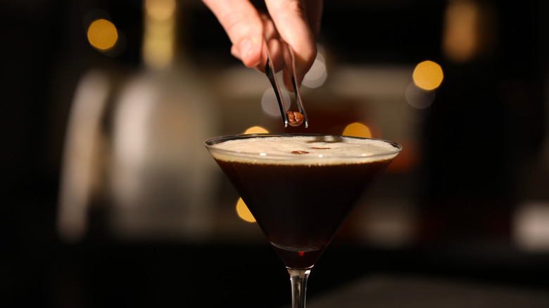 Hand holding small tongs and placing a coffee bean in an espresso martini