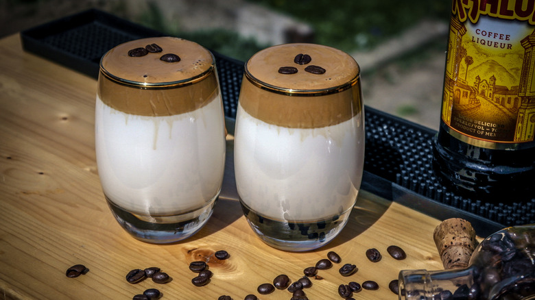 Two thick shake-like Kahlúa dalgona coffees sitting on a table next to a bottle of Kahlúa