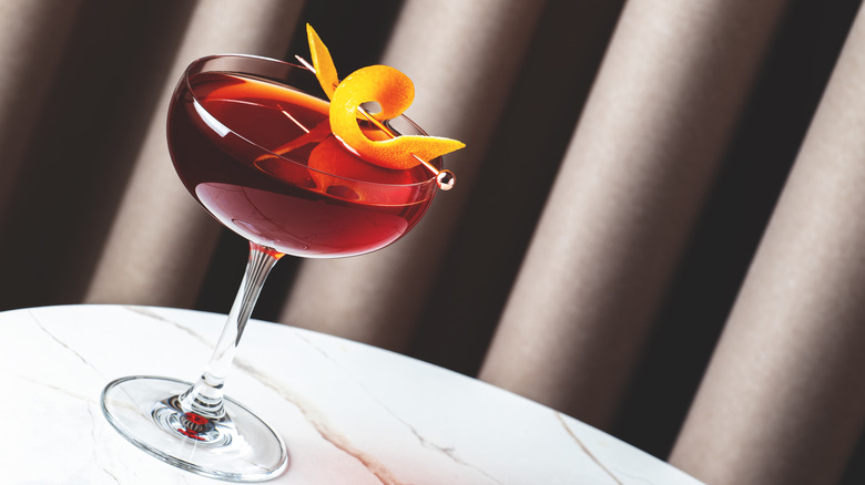 Revolver cocktail in a tilted martini glass with an orange peel on a plastic spear