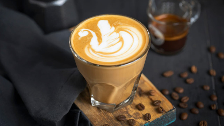 Creamy Spanish coffee sitting on a board with coffee beans next to a glass of coffee