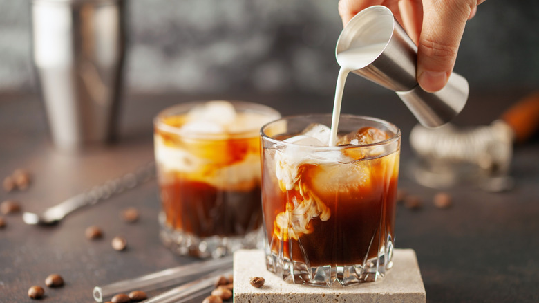 Cream being poured from a jigger into a glass for a white Russian cocktail