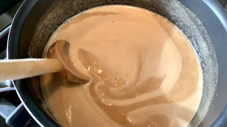 Person making caramel in a saucepan with a wooden spoon