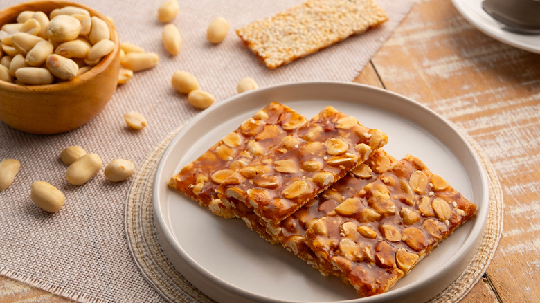 Peanut and sesame brittle on a plate next to small bowl of peanuts