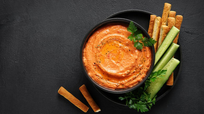 Orange dip in bowl with vegetables on a black background.