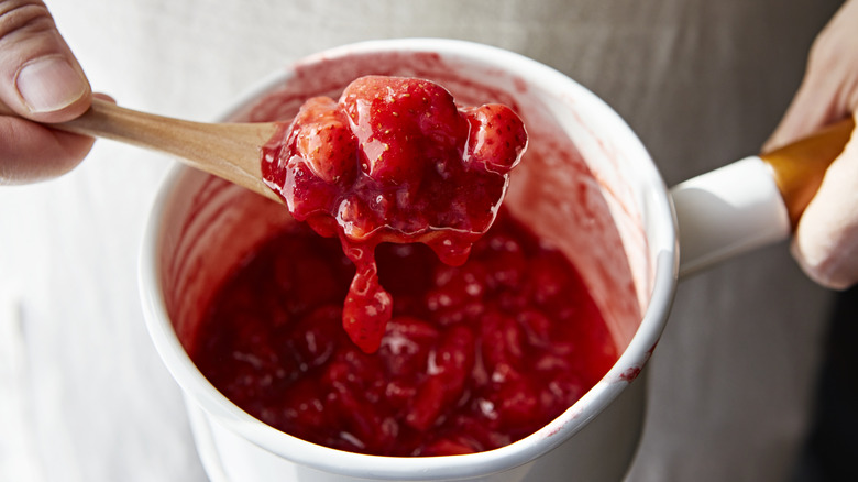 Person holding spoonful of strawberry jam from pot