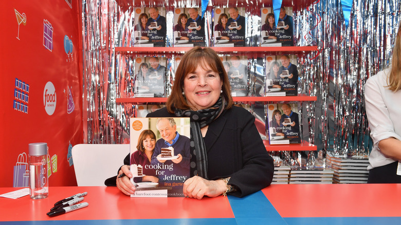 Ina Garten holding up the cookbook "Cooking For Jeffrey" and posing