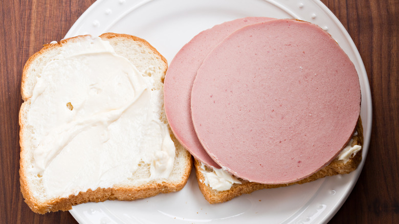 An overhead close up view of a white plate with an open face bologna sandwich