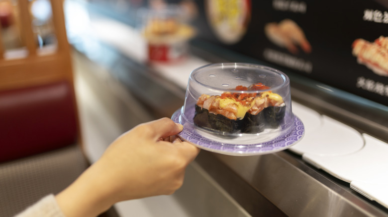 Person grabbing plate of sushi from conveyor belt