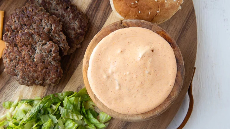 Aerial shot of special sauce on cutting board besides burgers