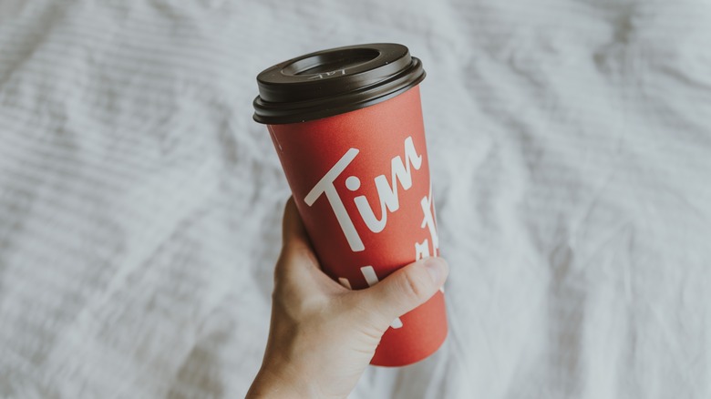 A hand holding a Tim Hortons takeout coffee cup