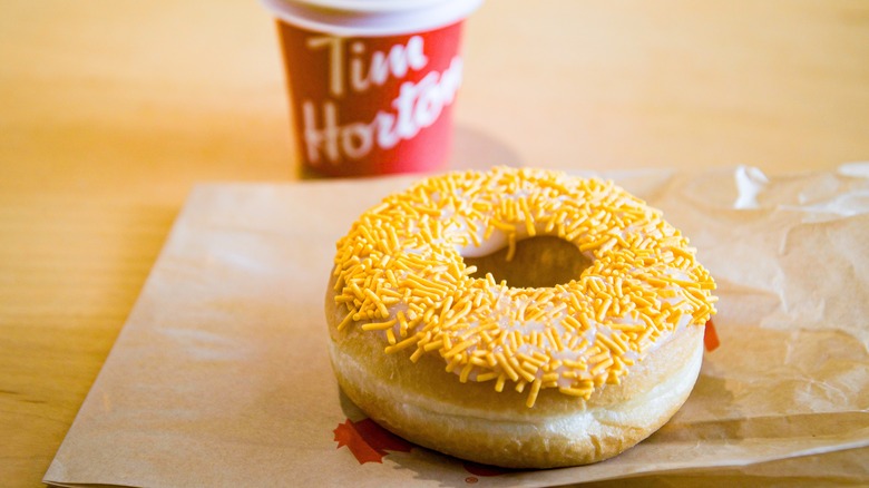 A donut with orange sprinkles and a cup of Tim Hortons coffee