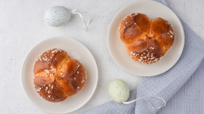 Two pinca breads on white plates next to Easter egg decorations