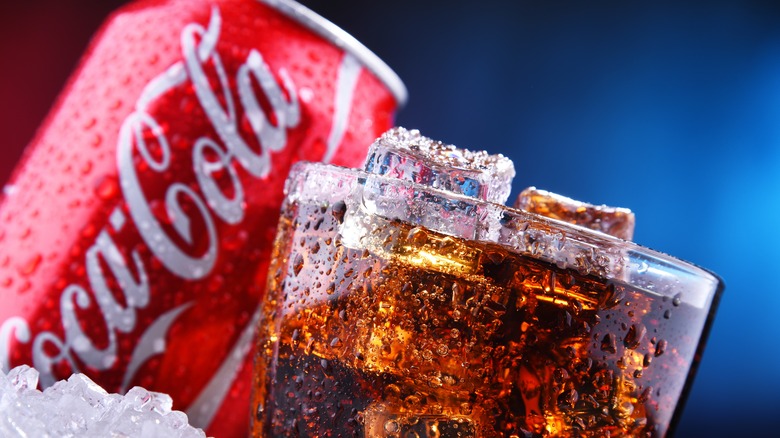 glass of iced coke with can in background