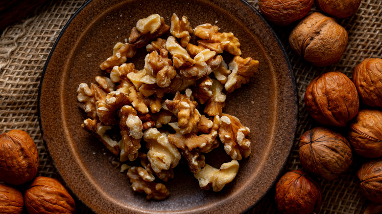 Walnuts in dish surrounded by shell-on walnuts