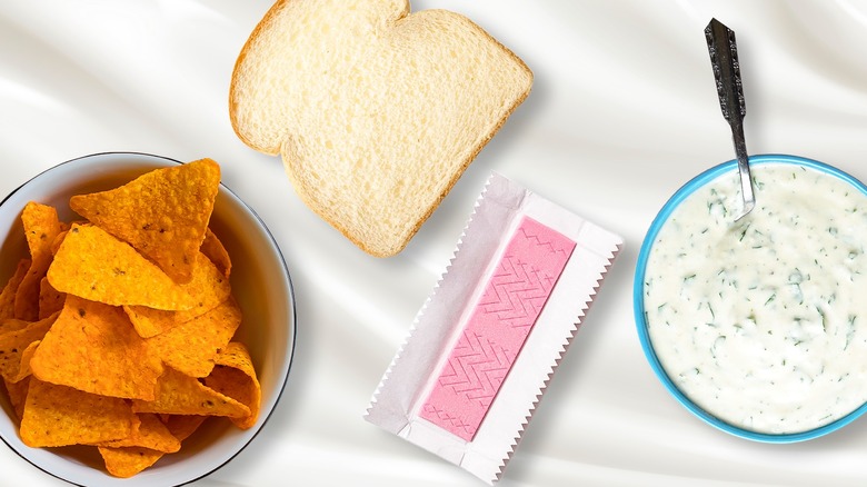 Potato chips in a bowl, slice of bread, stick of gum, and creamy dip in a bowl against a white background