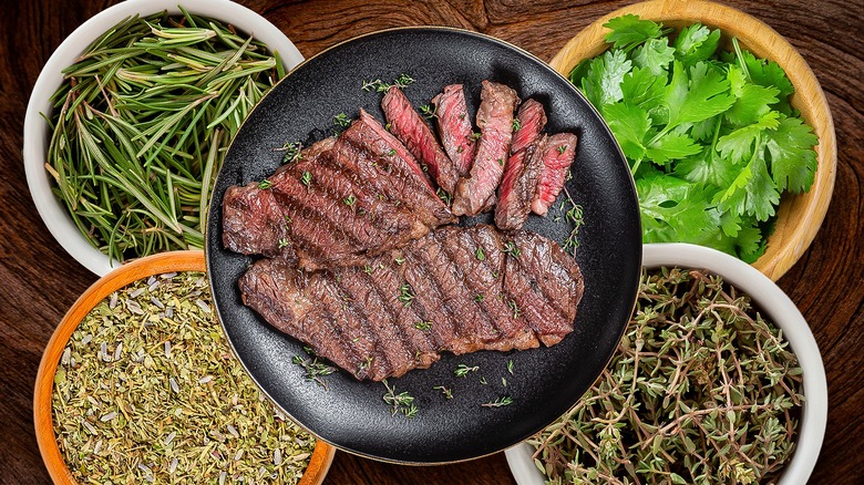 steak in the center plate surrounded by plates of fresh herbs