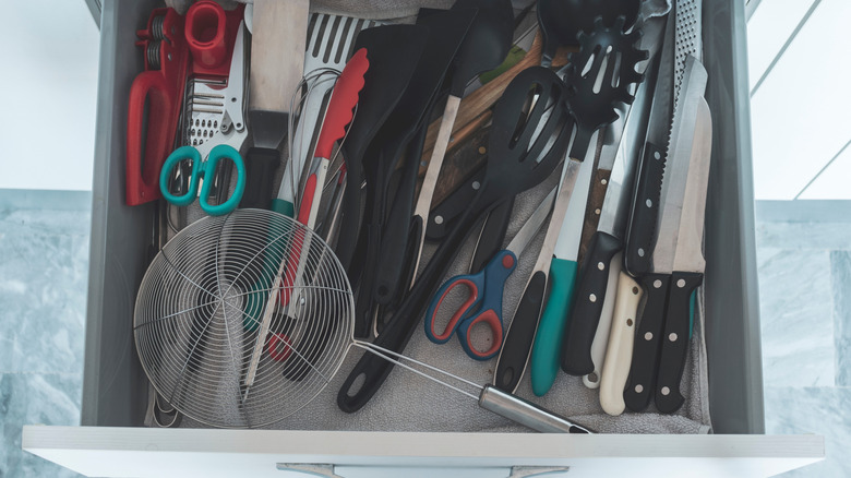 A disorganzied kitchen drawer with cooking utensils