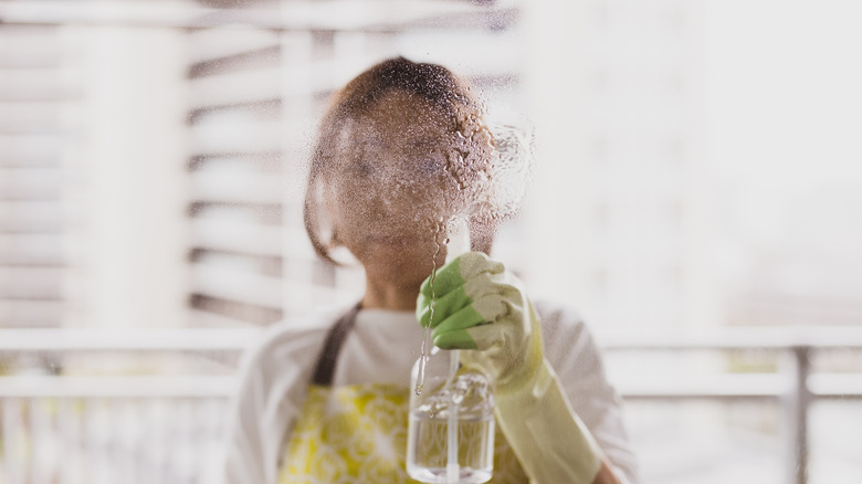 woman wearing rubber gloves cleaning a clear window using a spray