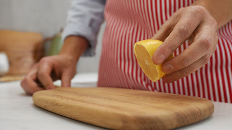 a person standing in the kitchen wearing an apron and cleaning a cutting board with lemon