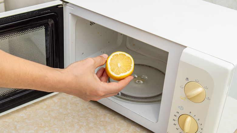 person placing half of lemon in a white dirty microwave sitting on a beige counter