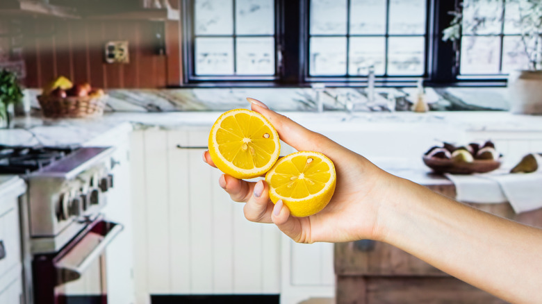 person holding two lemon halves with a classic kitchen blurred in the back