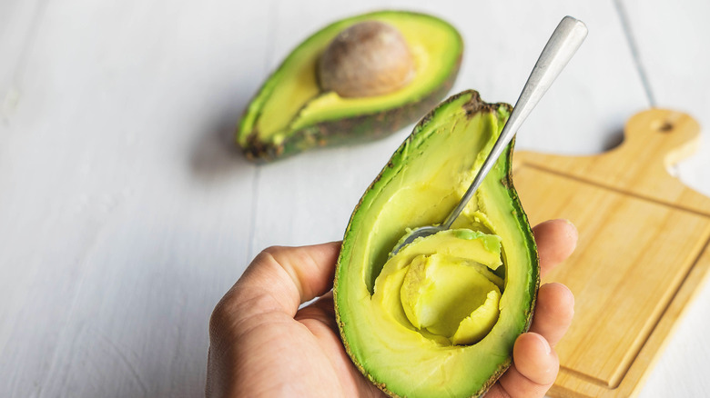 hand holding avocado with spoon