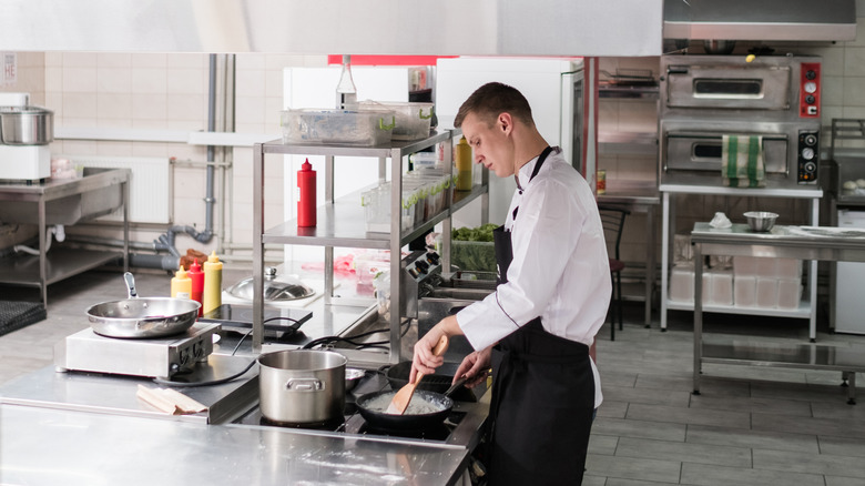 chef at stove in a professional kitchen stirring food in a cast iron skillet