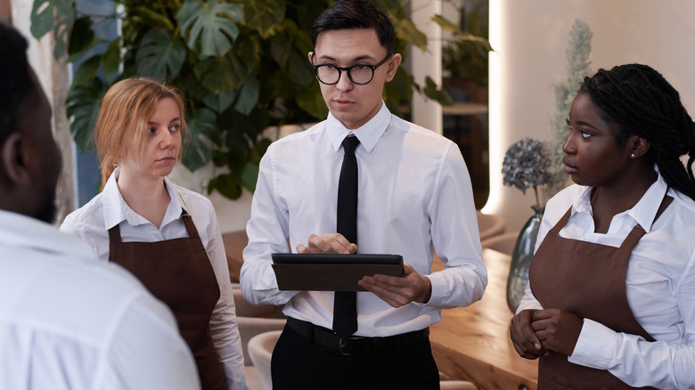 Restaurant manager holding a tablet in a discussion with the staff.