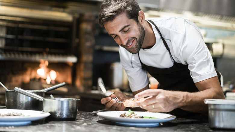 Smiling male chef plating food at restaurant.