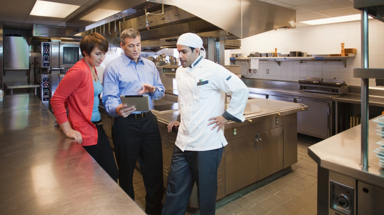 Manager holding a tablet talking with staff in the kitchen.