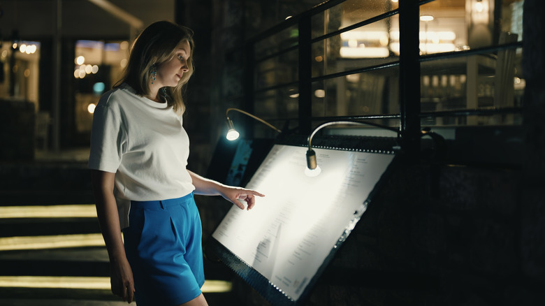 Woman looking at a menu before entering a restaurant.