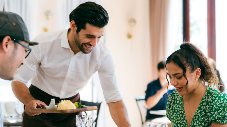 Waitstaff dropping off food to what appears to be happy guests.