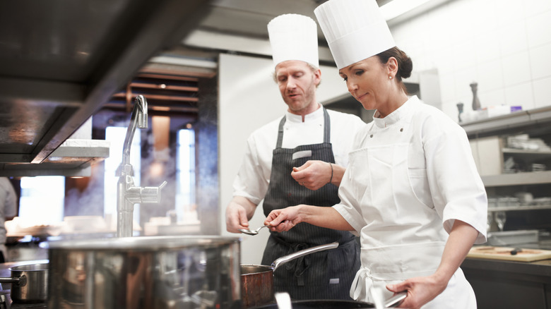 Head chef working with another chef in the kitchen at a stove.