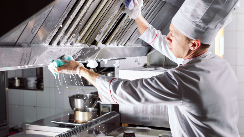 A chef meticulously cleaning his kitchen with a soapy sponge