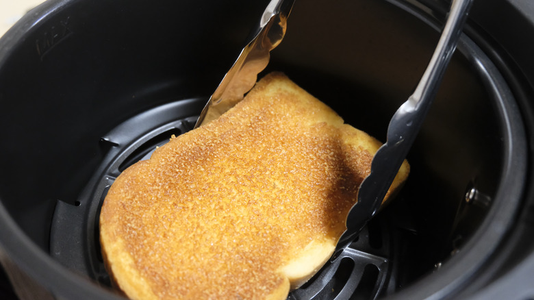 Tongs holding toast in air fryer