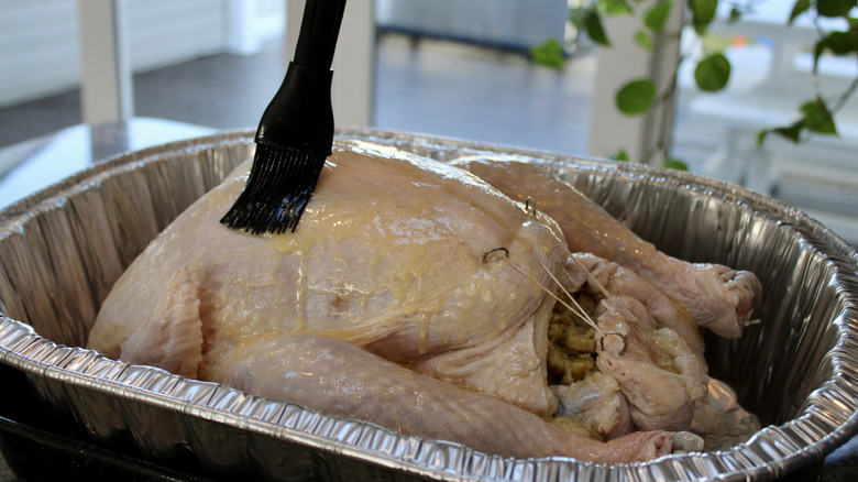 melted butter being brushed on raw turkey