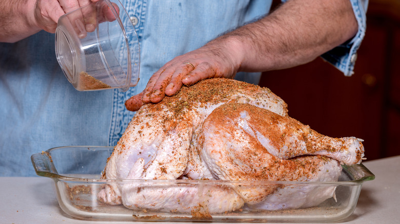 a person rubbing seasonings onto a whole turkey with their hand