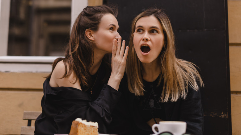 Two women interacting with each other outdoors in front of cup of drink