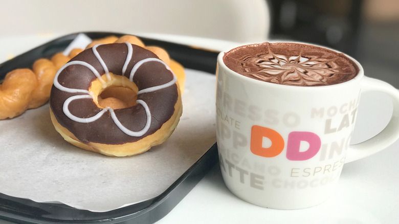 A mug of Dunkin latte with chocolate frosted donut on tray next to it