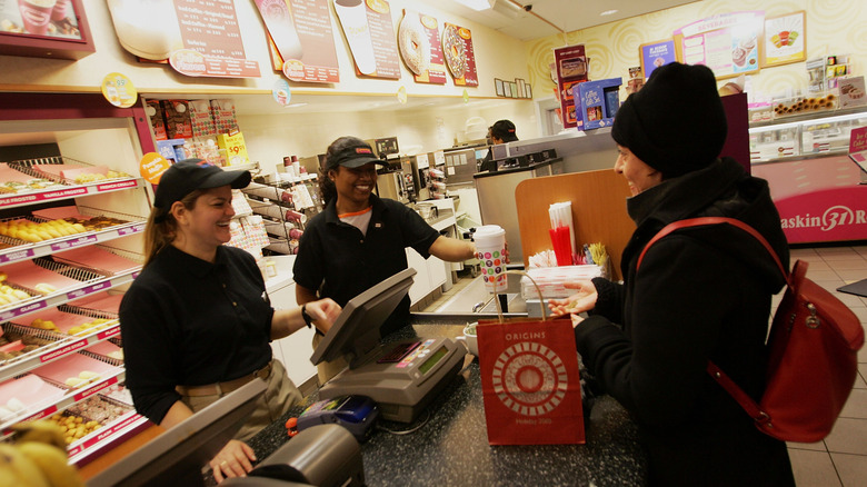 Two Dunkin' employees smiling at customer from behind the counter