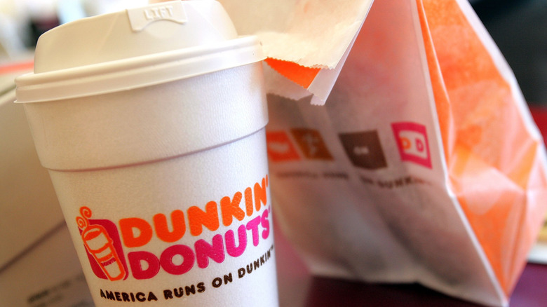 Closeup of a cup of Dunkin' hot coffee next to a Dunkin' bag