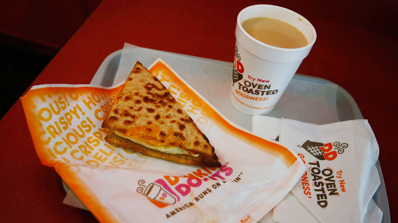 Dunkin' oven toasted egg sandwich on wrapper next to cup of beverage