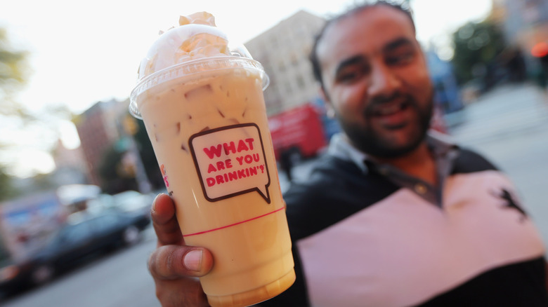 Man holding a cup of Dunkin' iced coffee with whipped cream outdoors