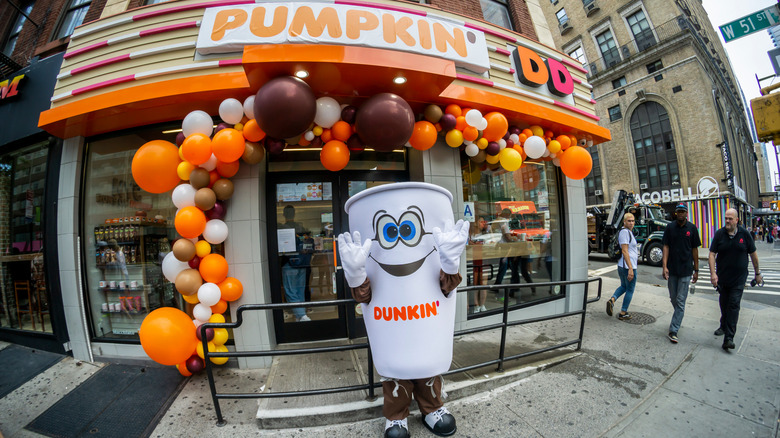 Dunkin' mascot outside of store front with seasonal signage and balloons