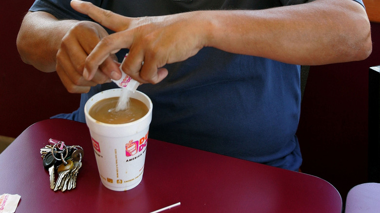 Person pouring sugar from a packet into Dunkin' hot coffee