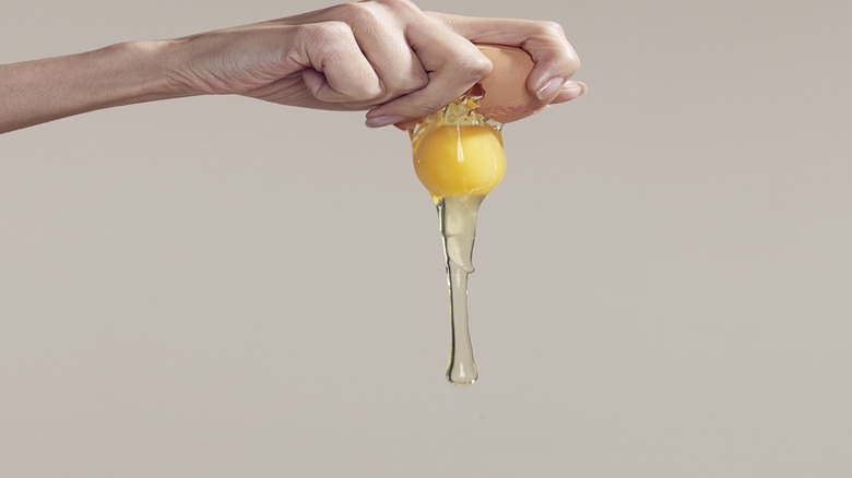 A close-up of someone cracking a brown egg with one hand