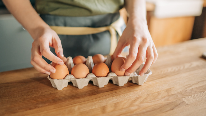 A person picking an egg from an egg carton sitting on a kitchen counter